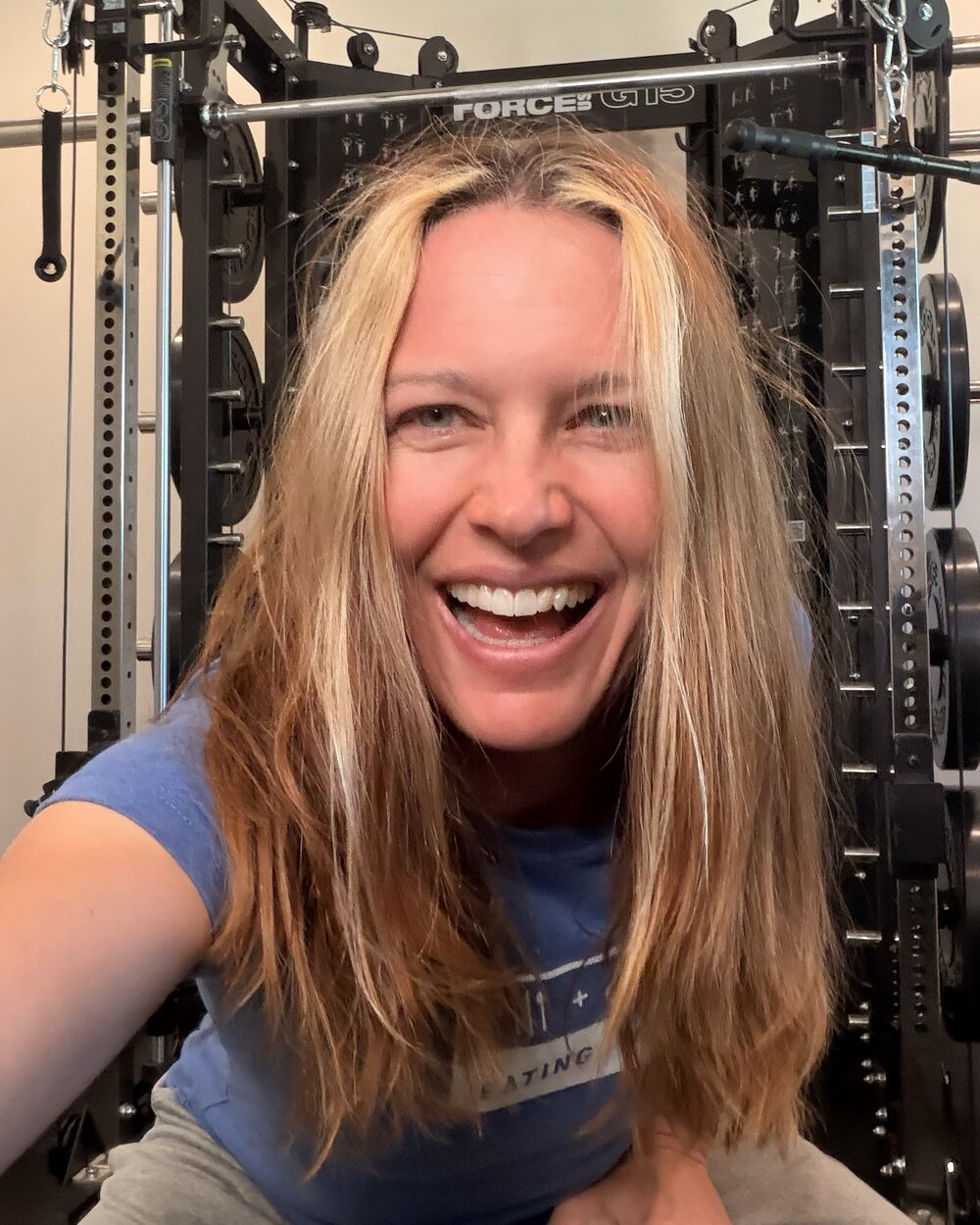 Kristina, the founder of Phaes, smiling in her home gym in front of a squat rack.